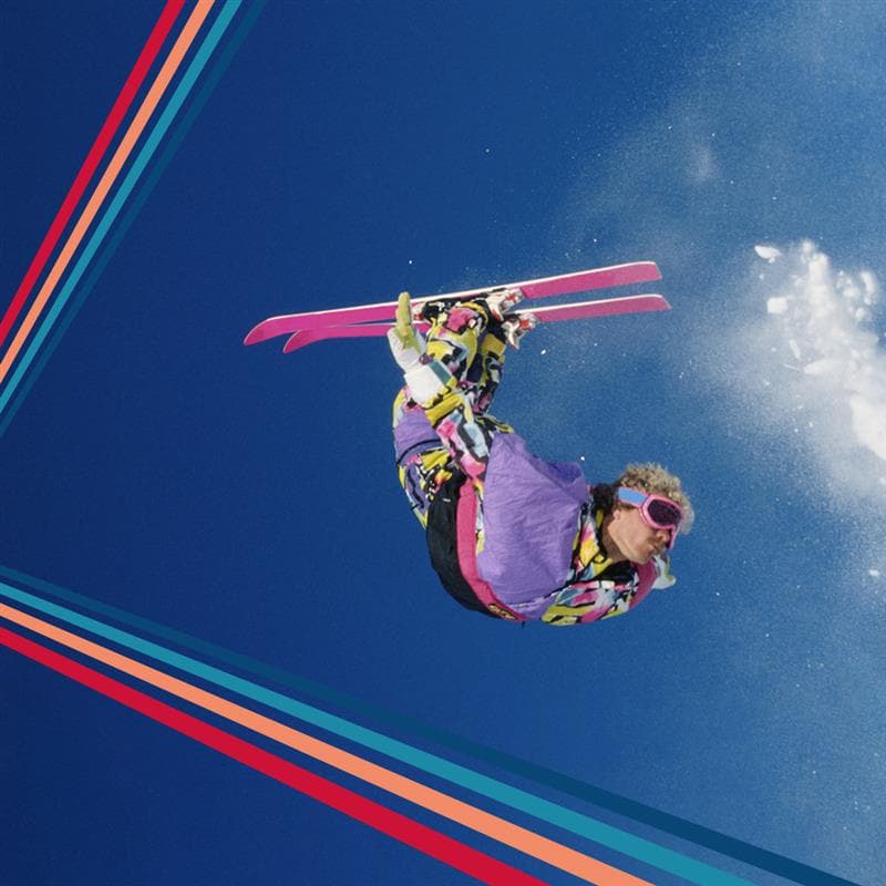 A skier in colorful gear performs an aerial flip against a clear blue sky, with dynamic diagonal stripes framing the image.