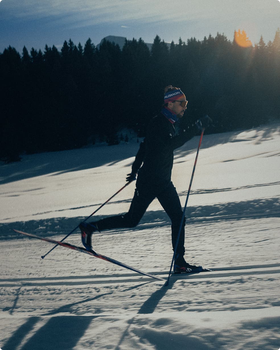 A person cross-country skiing on a snow-covered landscape with trees in the background