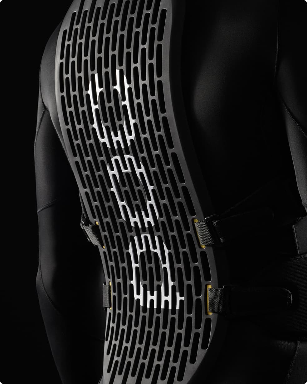 Back view of a person wearing a black protective spine guard with a grid pattern and white accents, set against a dark background.