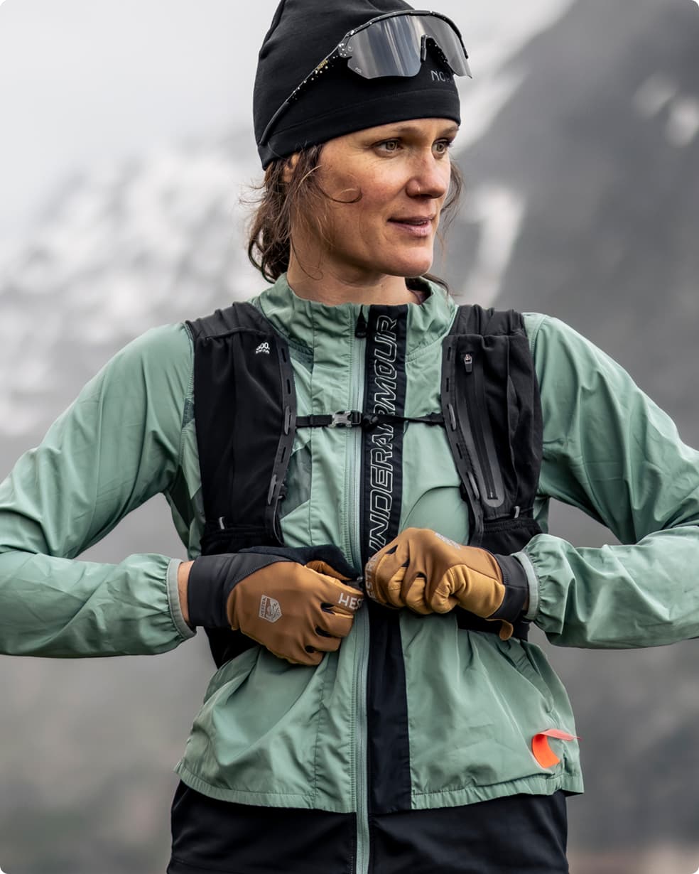 Person bundled in outdoor gear, adjusting equipment, with snow-capped mountains in the background, exuding a sense of adventure and resilience.